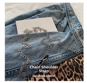 Close-up of leopard print crossbody bag with silver metal chain on denim background