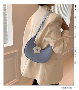 Detail of sky blue crescent underarm bag with a white flower charm and embossed logo
