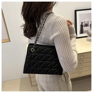Sac bandoulière noir matelassé avec chaîne dorée porté par un mannequin sur l'épaule