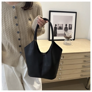 Minimalist black lychee texture bucket bag held by hand in a cozy lifestyle setting