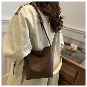 Close-up of brown litchi pattern leather bucket bag worn with a beige trench coat