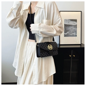 Detail of black crossbody bag with gold M logo and repeating pattern on a model