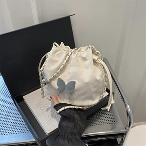 Sac seau en cuir blanc avec papillon argenté et bandoulière chaîne sur fond de décor moderne