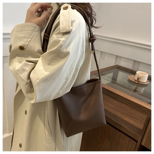 Detail of dark brown leather crossbody bucket bag with pebble texture and gold hardware