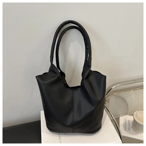 Close-up of black lychee texture leather bucket bag with long handles on white books