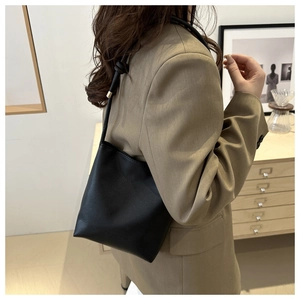 Detail of minimalist black pebbled leather bucket bag with gold-tone hardware and slim strap
