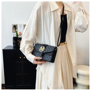 Detail of a black crossbody square bag with M-pattern print and golden metal clasp buckle