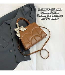 Detalle de bolso bandolera marrón acolchado con pañuelo decorativo sobre blazer oscuro