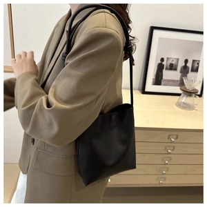 Minimalist black faux leather bucket bag with slim shoulder strap shown on a casual blazer