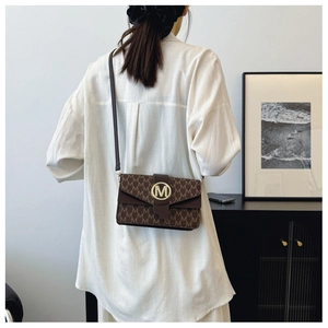 Rear view of a model wearing a brown monogram crossbody bag with a gold M logo clasp