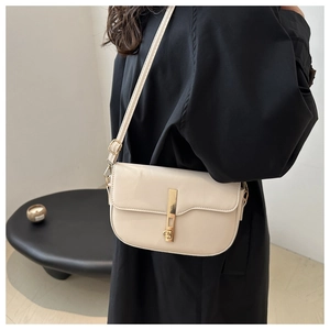 Detail of minimalist beige saddle bag with gold metal lock worn over a black coat
