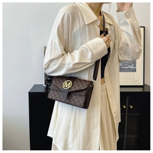 Detailed view of the brown shoulder bag with monogram print and golden M buckle on model