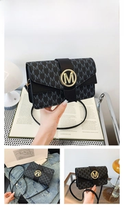 Detail of black underarm bag featuring M-pattern texture and gold metal buckle