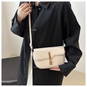 Detail of cream leather saddle bag featuring a sleek golden metal bar lock and strap