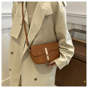 Detailed view of brown leather saddle bag with long vertical metal lock on trench coat