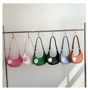 Row of colorful crescent shoulder bags with floral charms hanging on metal display hooks
