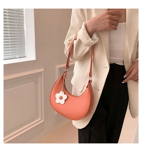 Orange PU leather crescent shoulder bag featuring a small white flower charm on model