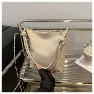 Detail of cream white pebbled leather bucket bag featuring knotted strap and metal seal