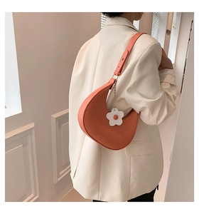 Detail of bright orange crescent shoulder bag with white flower charm on white blazer