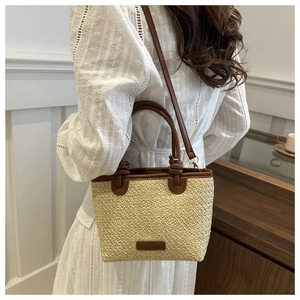 Détail du sac cabas en paille tissée avec poignées en cuir marron et bandoulière réglable
