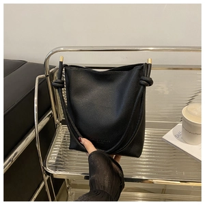 Detail of black lychee grain leather bucket bag with gold accents and knotted strap