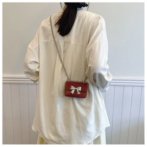 Détail d'un mini sac bandoulière en cuir rouge avec nœud argenté et bandoulière chaîne