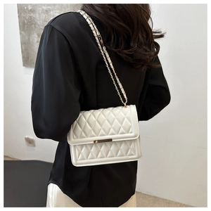 Close-up of a white quilted crossbody bag with golden chain and metallic buckle detail
