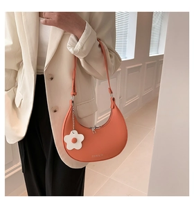 Close-up of orange crescent shoulder bag with white flower charm and silver zipper