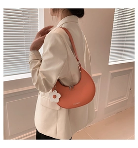 Detail of orange crescent shoulder bag with white flower charm on beige blazer