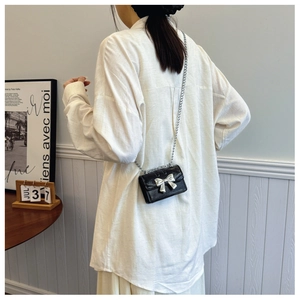 Mini black crossbody bag with silver butterfly bow shown worn by a model in a retro setting