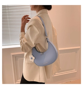 Detail of light blue crescent shoulder bag with matte texture and floral charm accessory