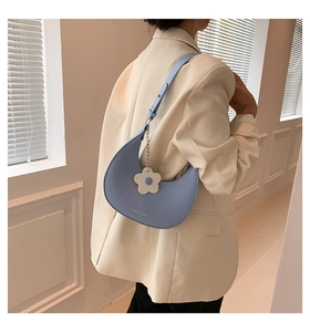 Close-up of light blue crescent underarm bag with white flower charm and leather texture