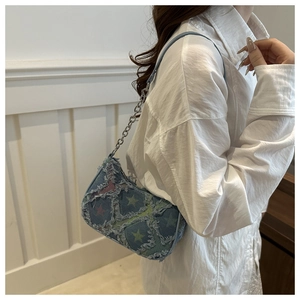 Close-up of light blue denim star-patterned baguette bag with trendy distressed frayed edges