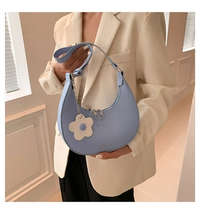 Close-up of a light blue crescent moon bag with a white flower charm and logo detail