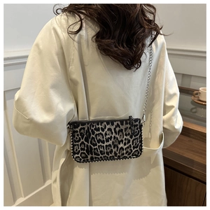 Detail of leopard print shoulder bag with silver studs and chain strap on a model