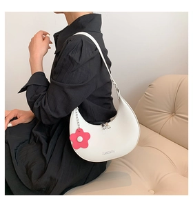 Close-up of white half-moon shoulder bag with pink flower charm and dual zippers