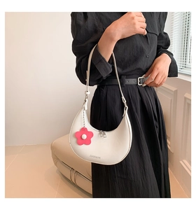 Detail of off-white crescent moon bag featuring a red floral charm and brand lettering
