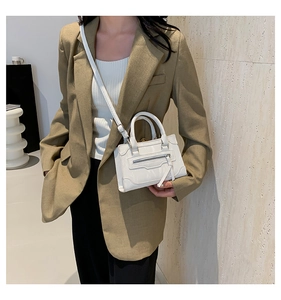 Close-up of white glossy crossbody bag with zipper detail on a brown blazer outfit