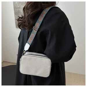 Close-up of white crossbody bag with rose floral embossing and colorful woven strap