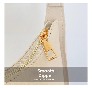 Detail of smooth gold zipper and clean stitching on a creamy white shoulder bag