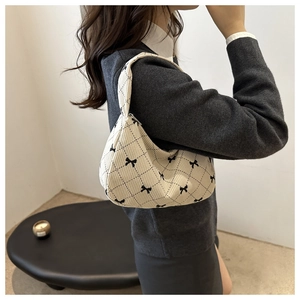 Detail of a beige quilted shoulder bag with black bows and jacquard fabric texture