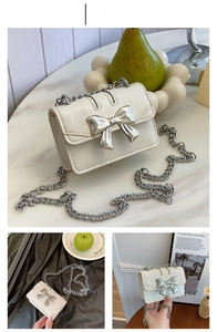 Detail view of mini cream crossbody bag featuring a large silver metallic bow and chain