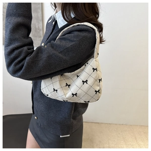 Detail of cream shoulder bag featuring black bow patterns and textured fabric texture