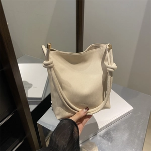 Minimalist beige pebble leather bucket bag with knotted rope handle and gold metal caps