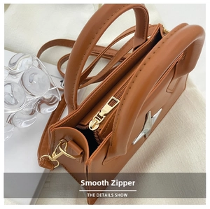 Detail view of smooth metal zipper and silver star ornament on brown leather bag