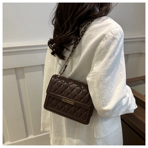 Detail of dark brown quilted crossbody bag with gold hardware worn by a model
