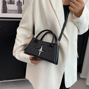 Detailed view of mini black square bag with silver star metal accent on white blazer