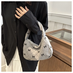 Close-up of gray corduroy handbag with black bow patterns and elegant metal zipper details