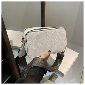 Detail of white leather camera bag with floral embossing and ethnic wide strap