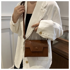 Dettaglio di una borsa a tracolla vintage marrone con finitura opaca su giacca bianca